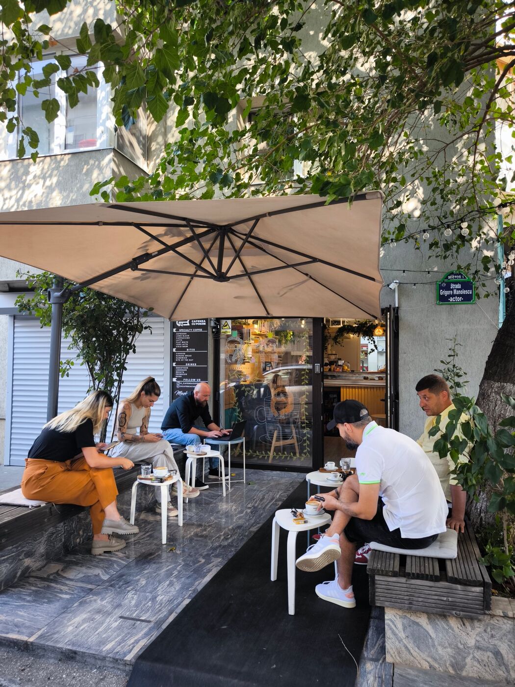 Terasa cafenelei, cu oameni la cafea sub umbrelă